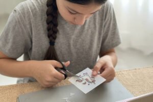 ילדה גוזרת מדבקות חד קרן בפעילות יצירה בבית